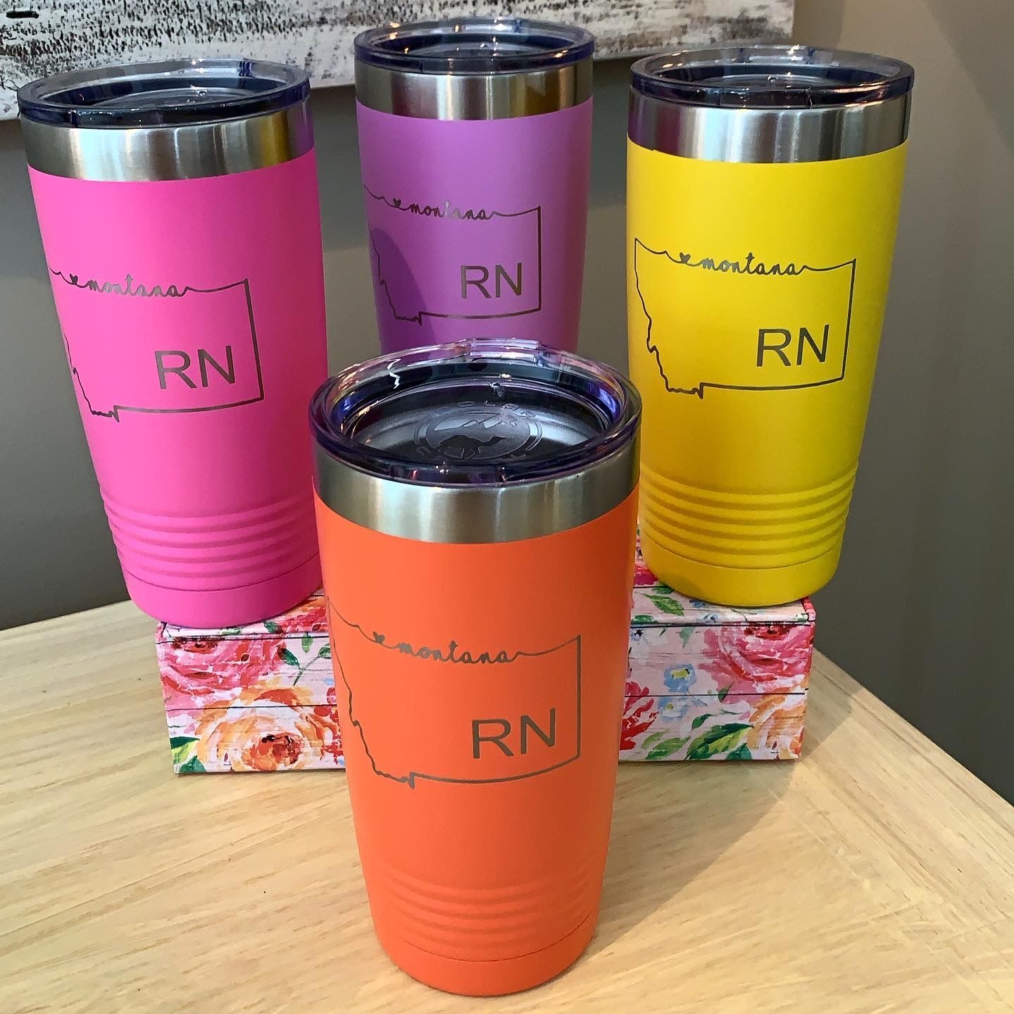 Four different colored tumblers with rn written on them are sitting on a wooden table.
