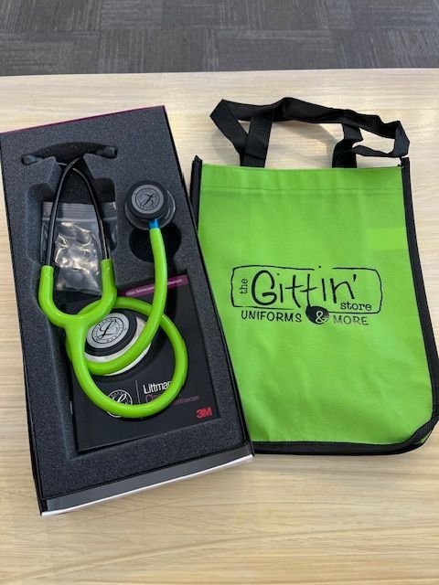 A green stethoscope is in a box next to a green bag