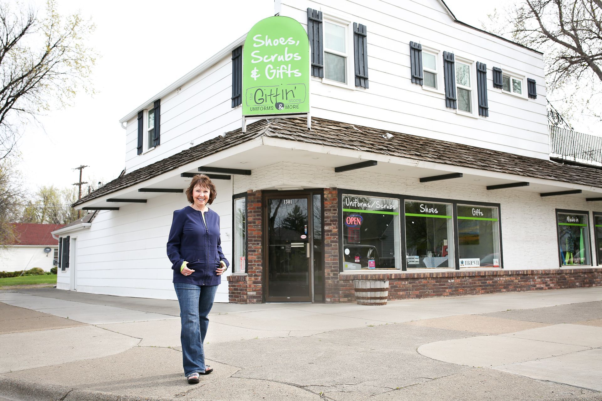 A woman is walking in front of a store that sells shoes sunglasses and gifts