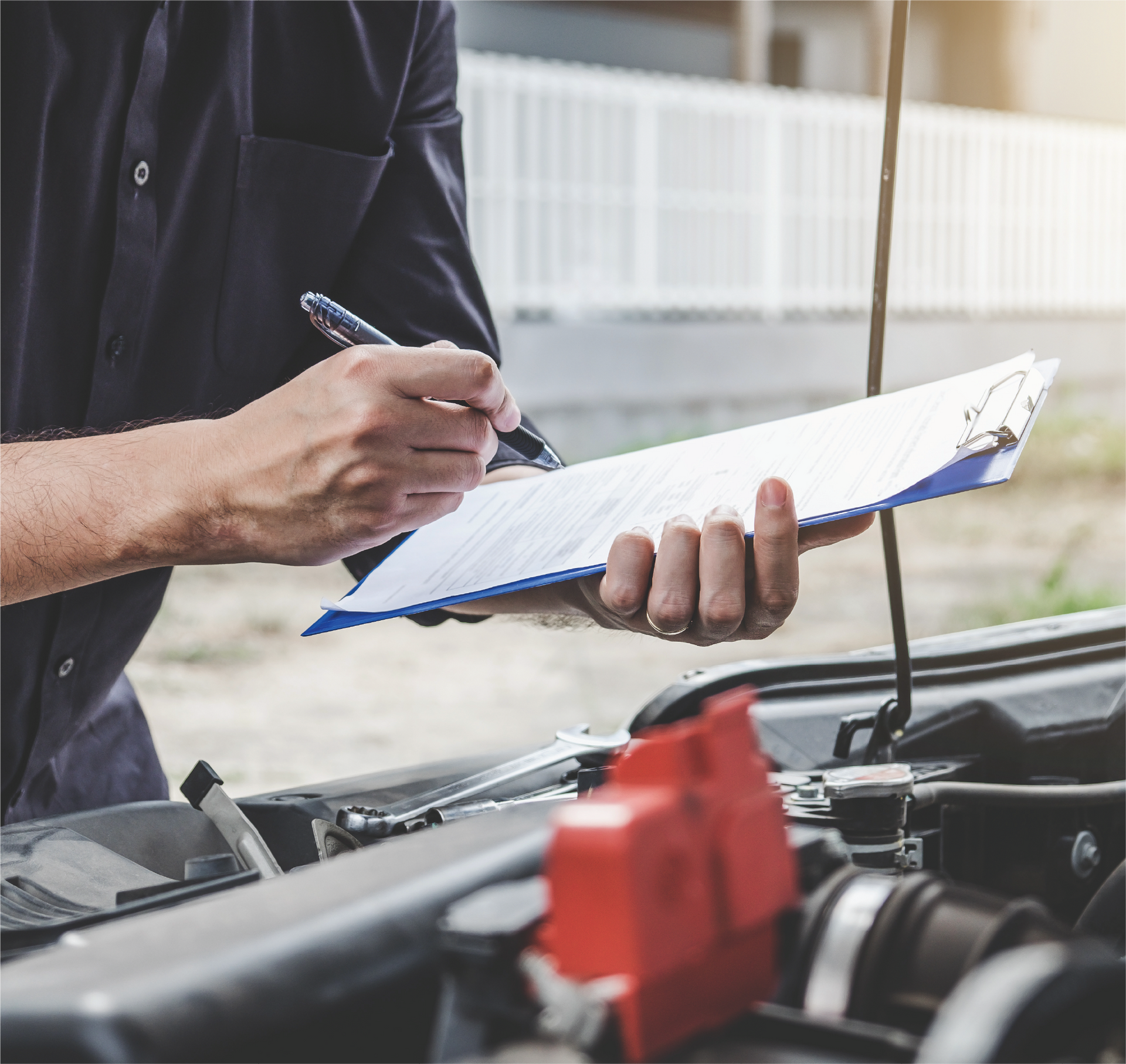 A man is writing on a clipboard while looking under the hood of a car.