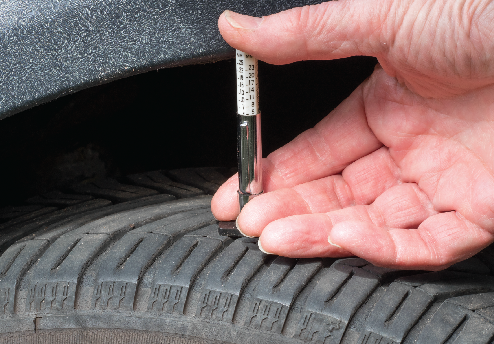 A person is measuring the depth of a tire with a gauge.