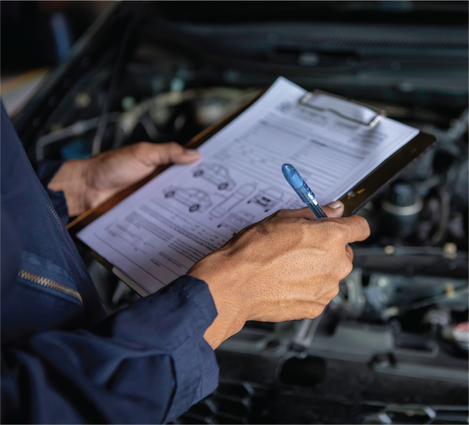 A man is holding a clipboard and a pen in front of a car engine.