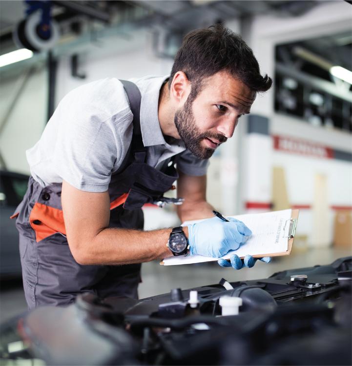 A man is looking under the hood of a car while holding a clipboard.