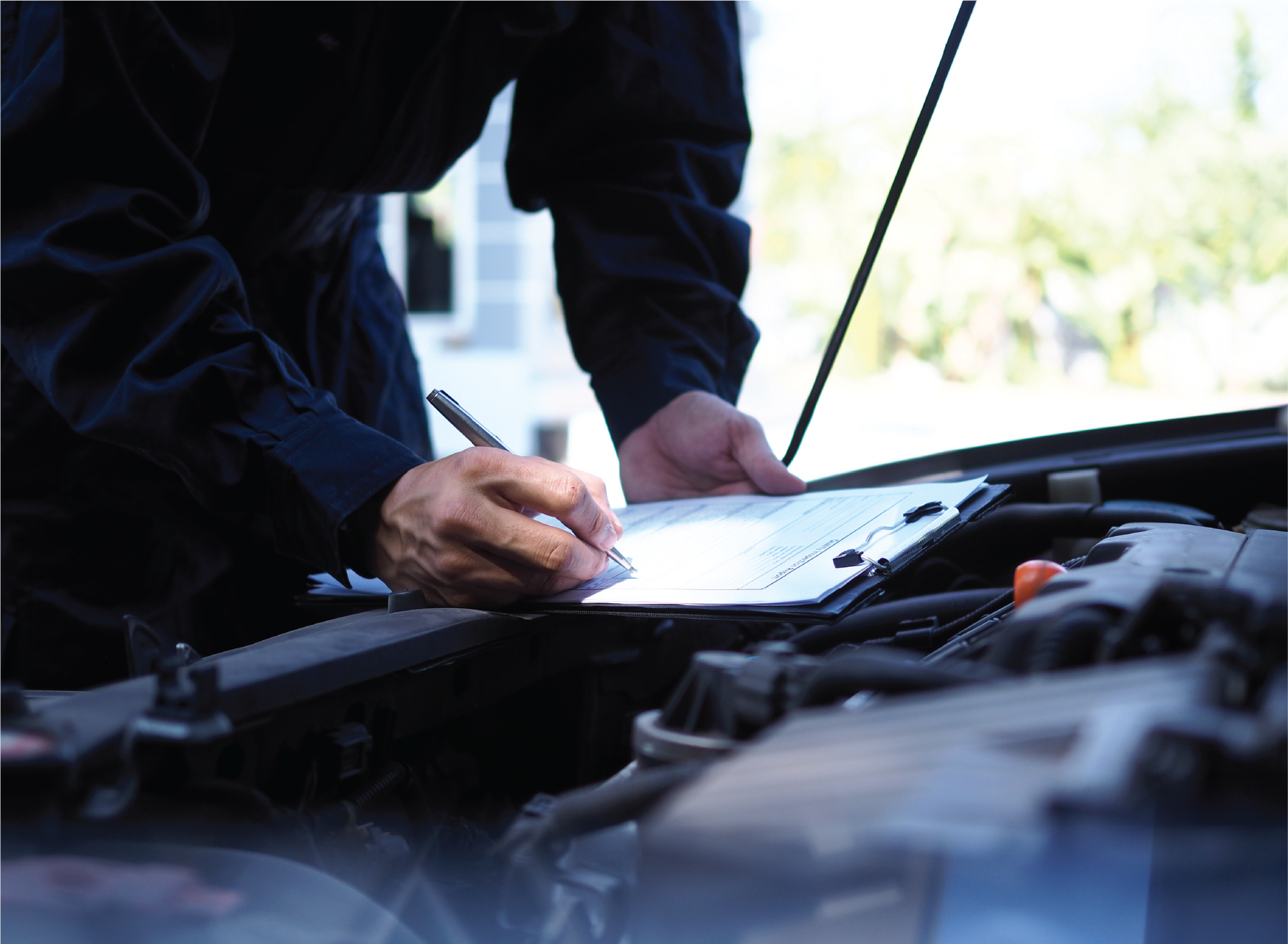 A man is writing on a clipboard under the hood of a car.