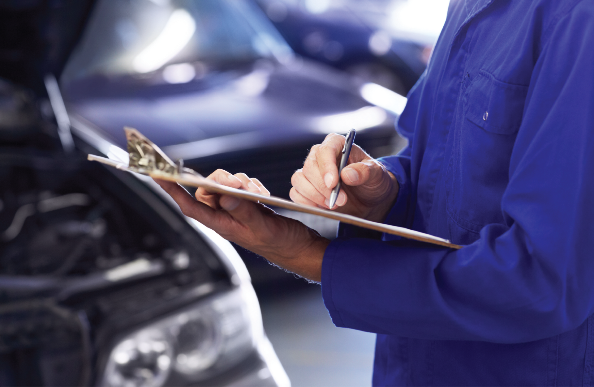 A mechanic is writing on a clipboard in front of a car.