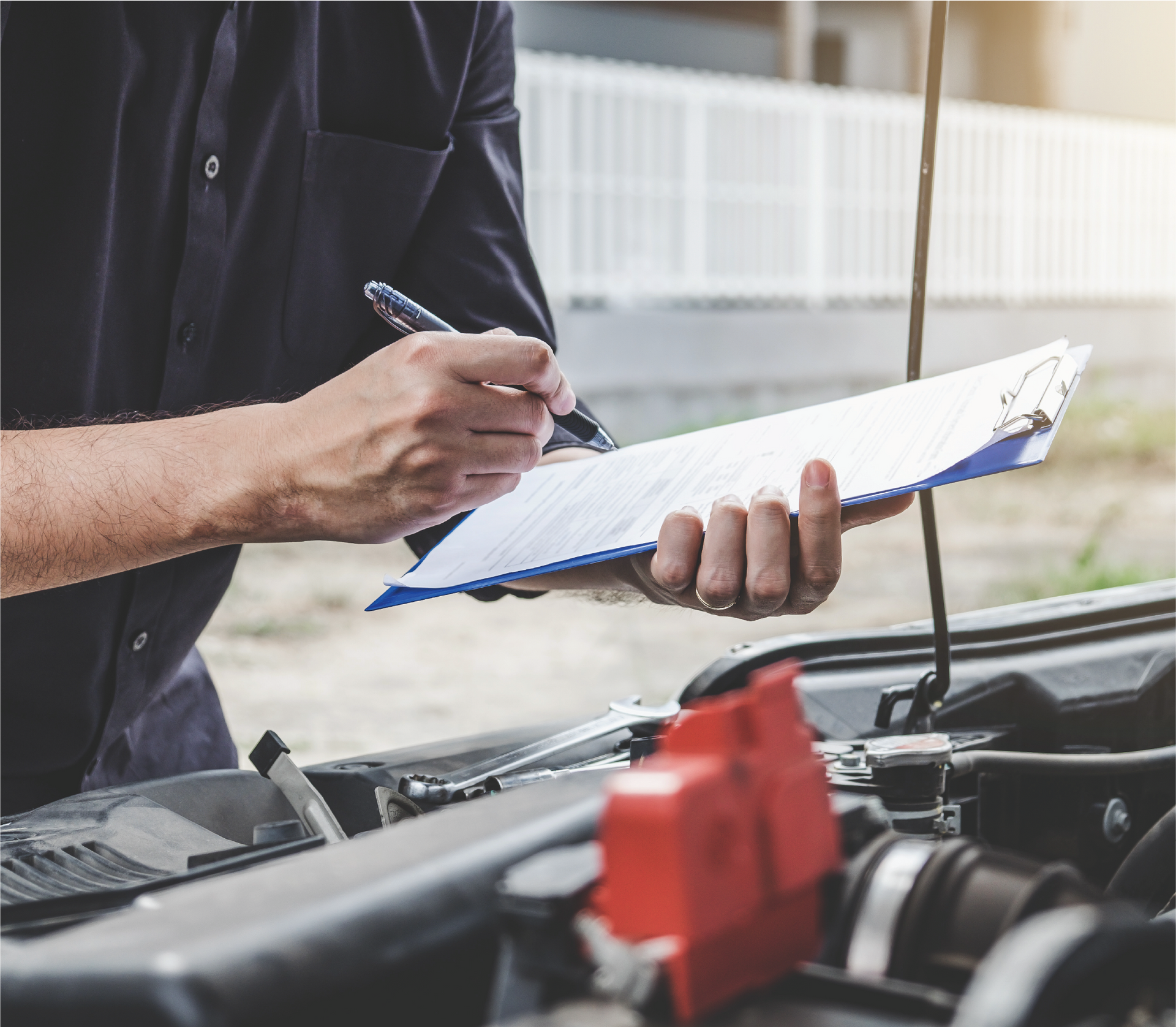 A man is writing on a clipboard while looking under the hood of a car.