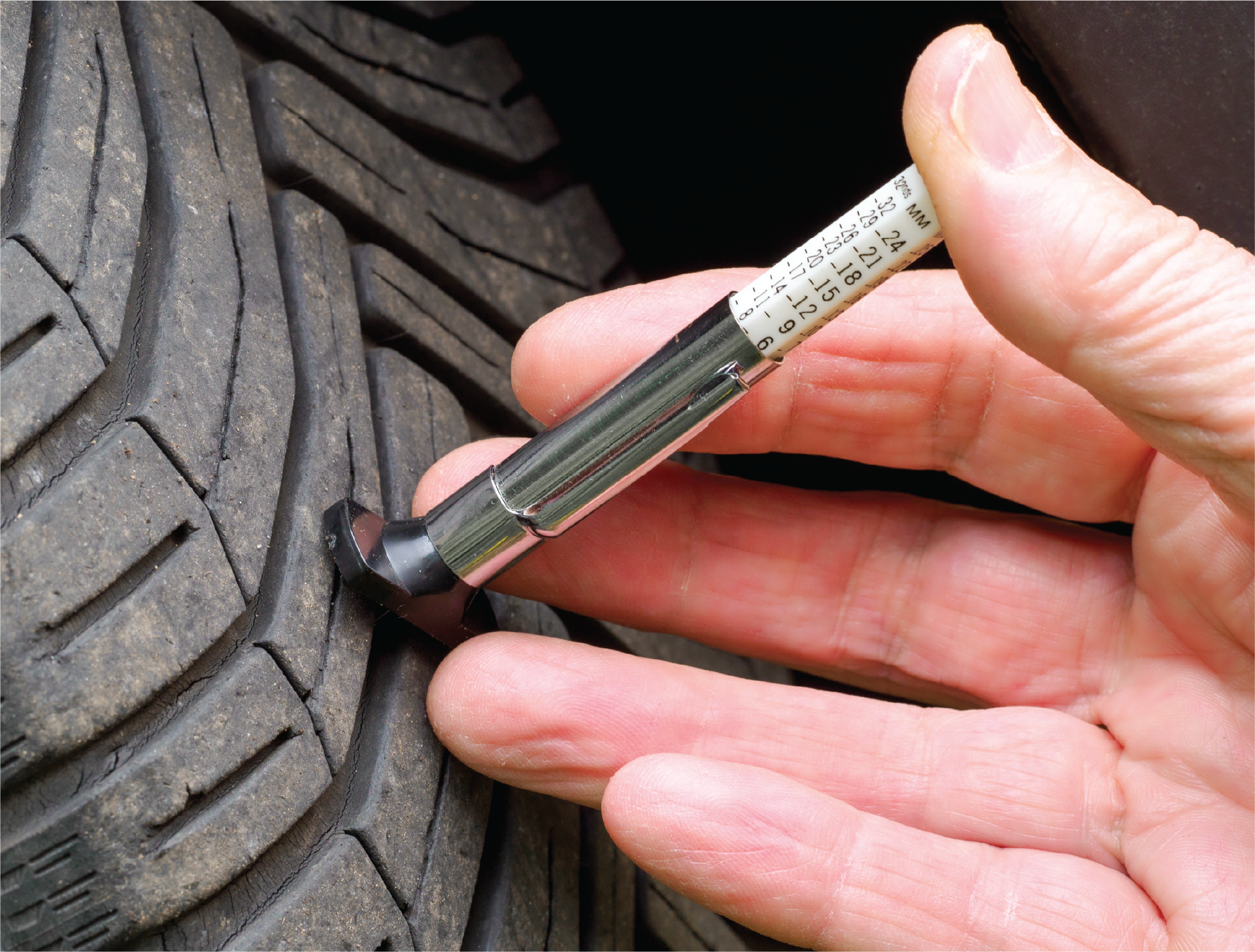 A person is measuring the depth of a tire with a pen