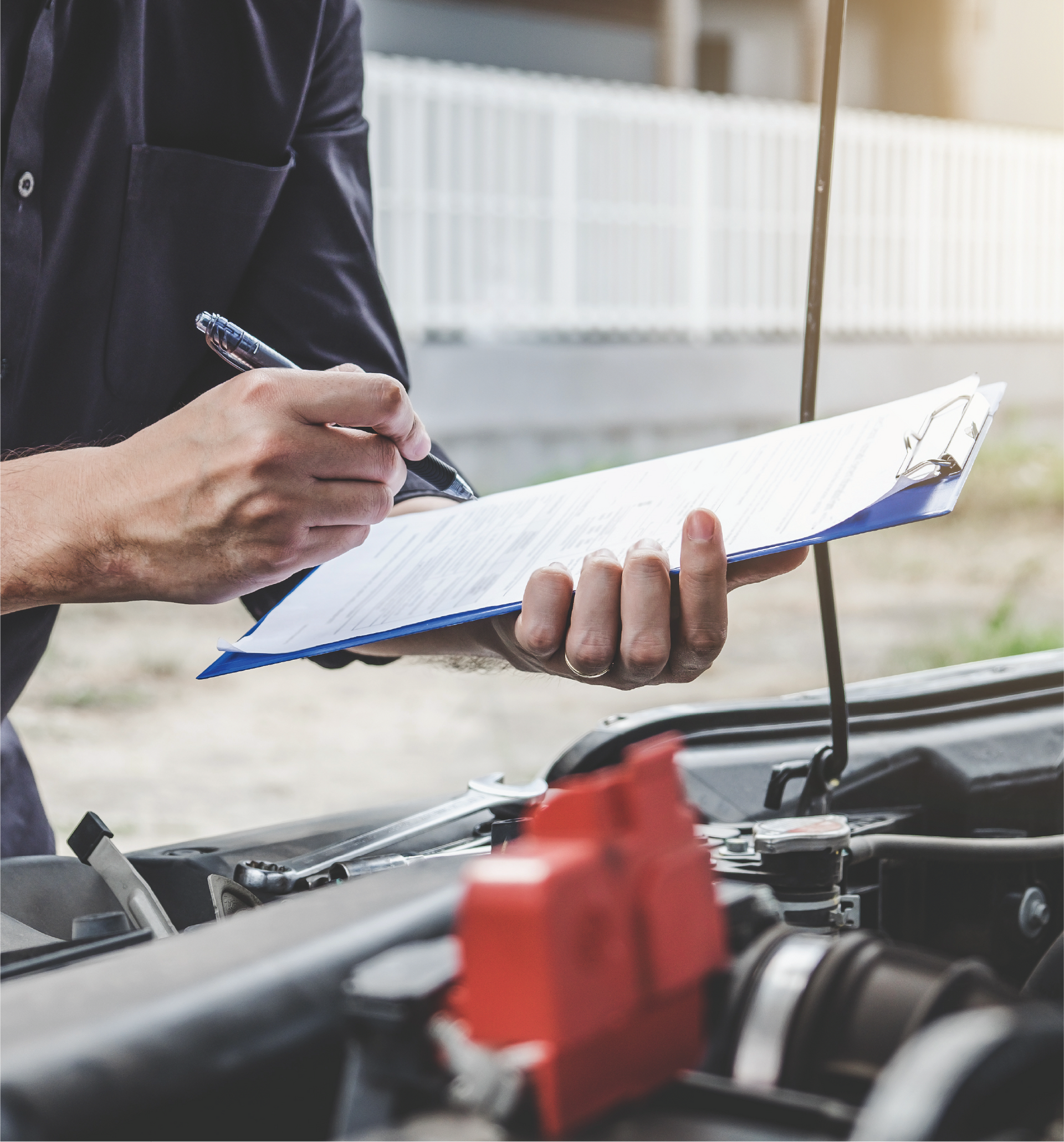 A man is writing on a clipboard while standing next to a car.