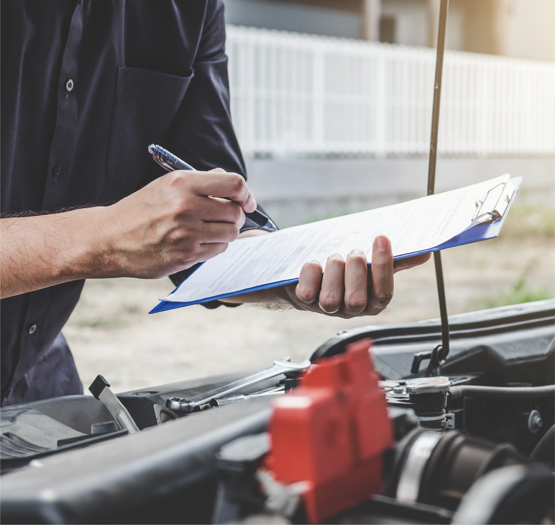 A man is holding a clipboard and writing on it while working on a car.