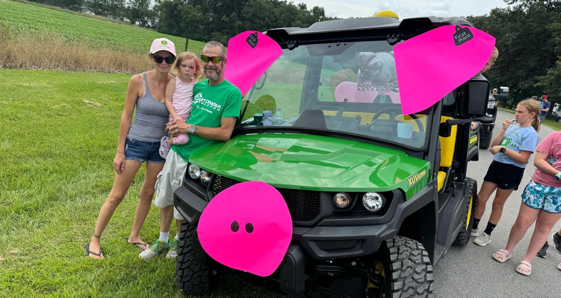 A family poses next to a John Deere Gator that is decorated as a pig.