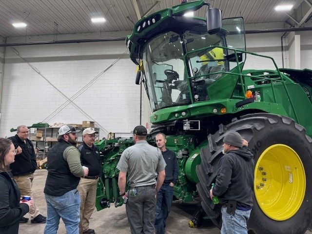 a group of customers and employees gather around a John Deere self-propelled forage harvester