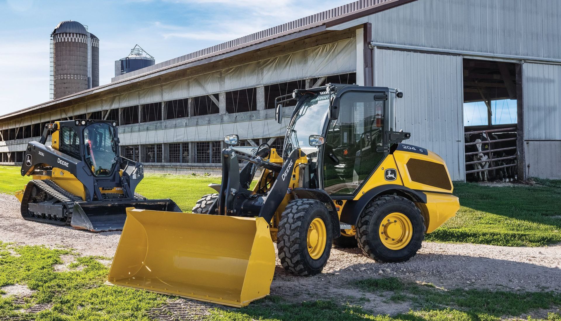 John Deere compact construction equipment parked outside of a dairy barn