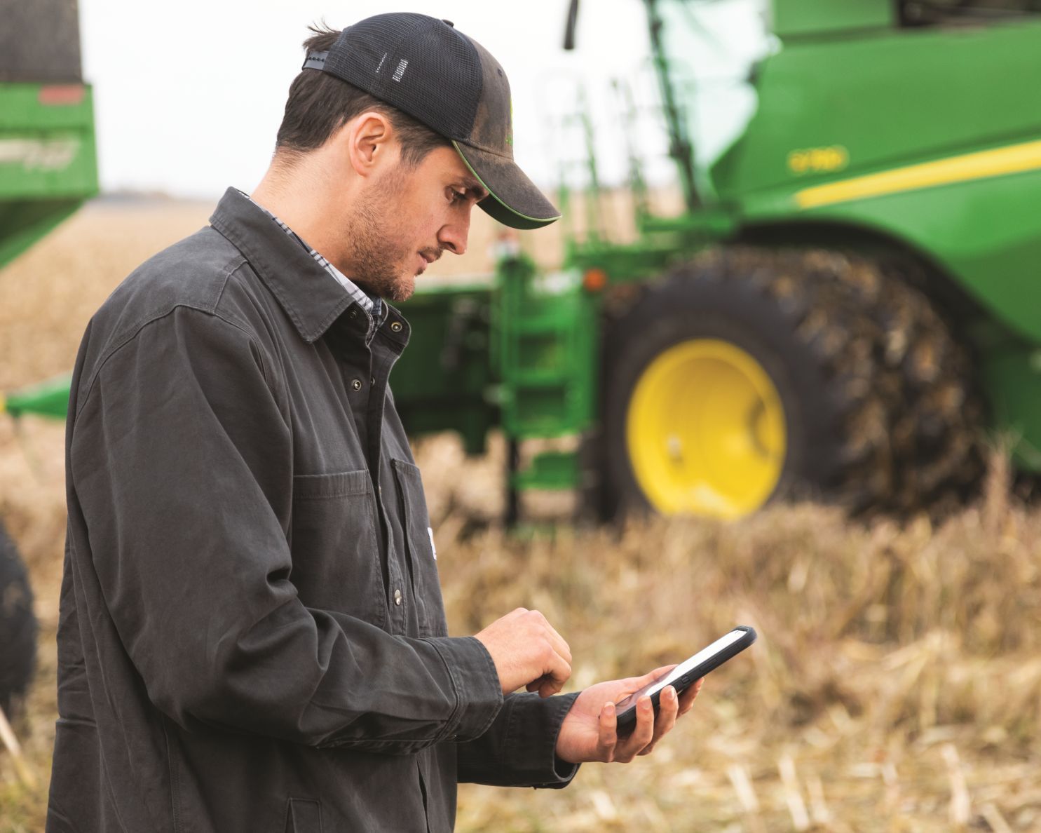 Man looks at a cell phone while standing in a field near a combine harvester