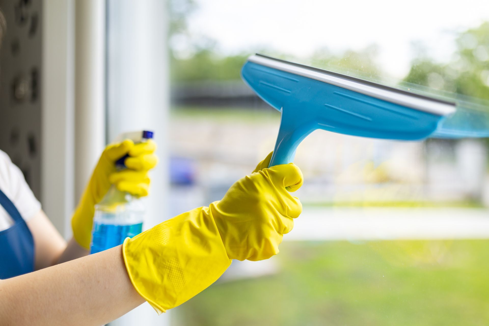 Janitor a window with a squeegee and spray cleaner, showcasing house cleaning services.
