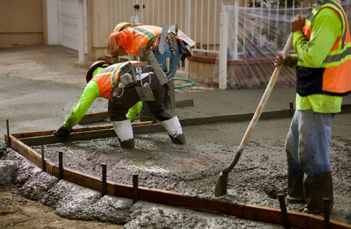 Construction workers pouring and smoothing concrete, wearing safety vests and using tools outdoors.