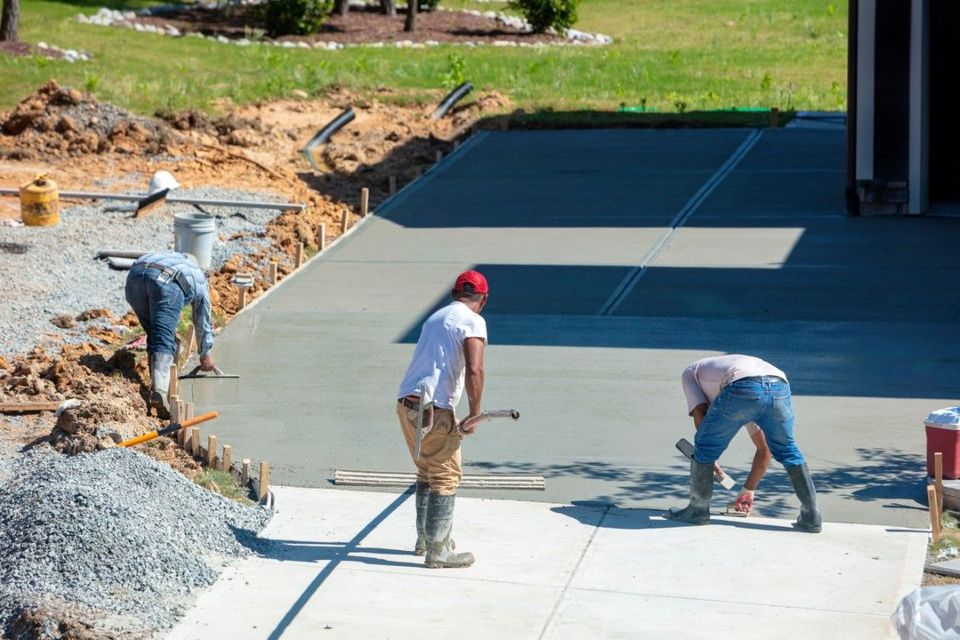 Construction workers smoothing wet concrete on a driveway in front of a house.
