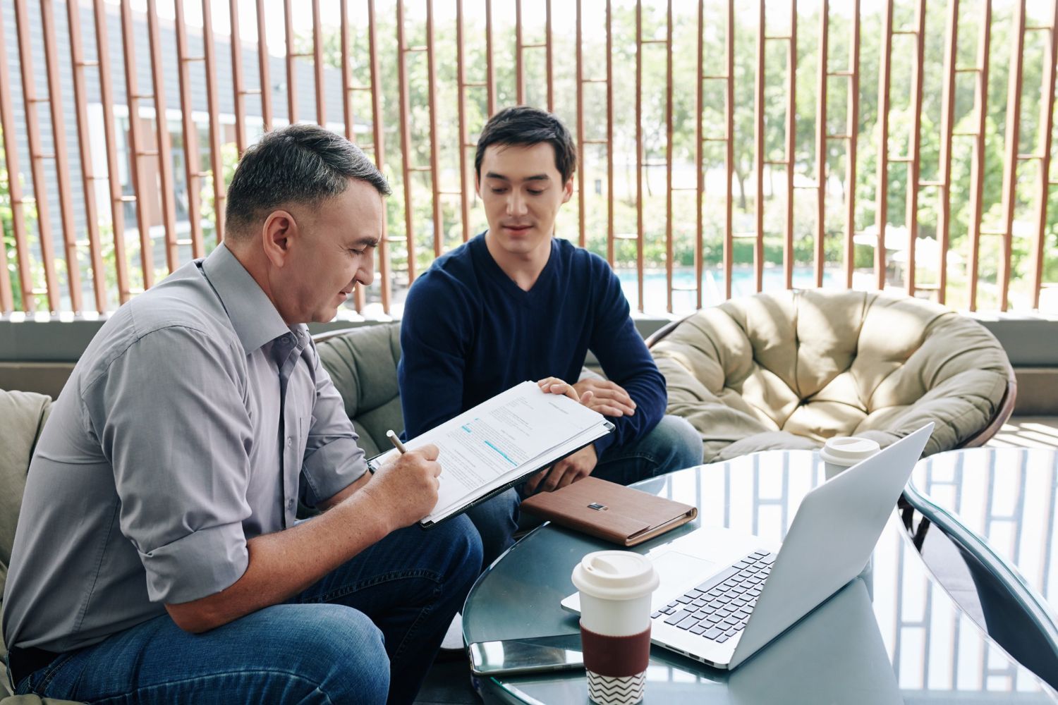 Two men in an office setting reviewing documents. One man is signing a document while the other observes.
