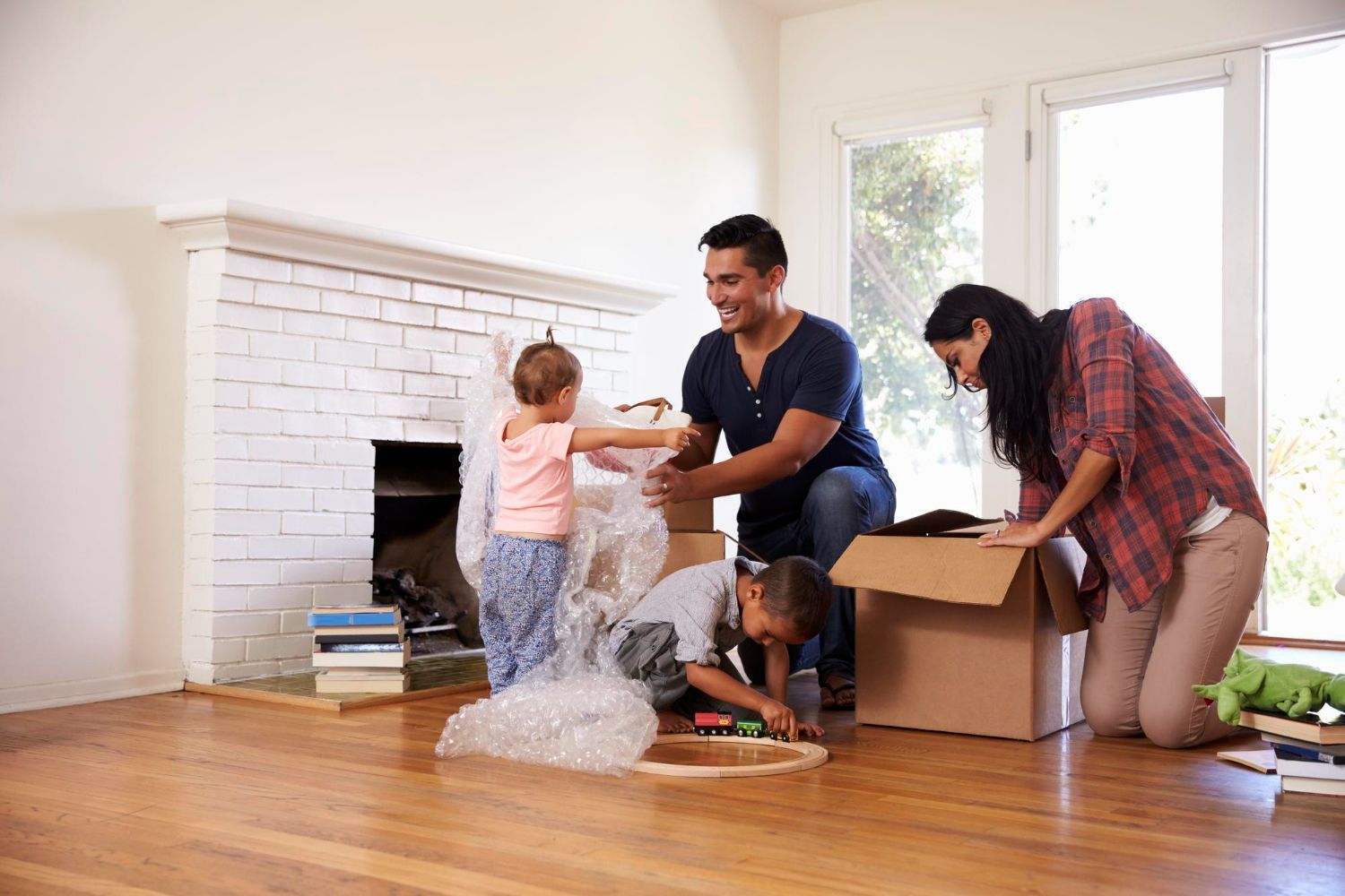 Family unpacking boxes in a new home, children playing with bubble wrap, smiling.