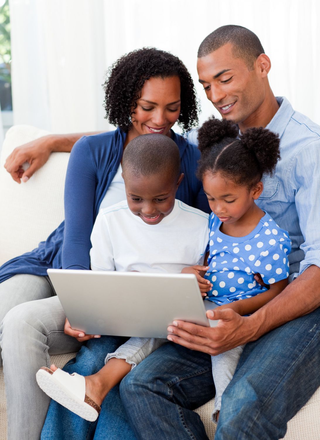 Family of four on couch looking at a laptop; parents smiling, children focused.