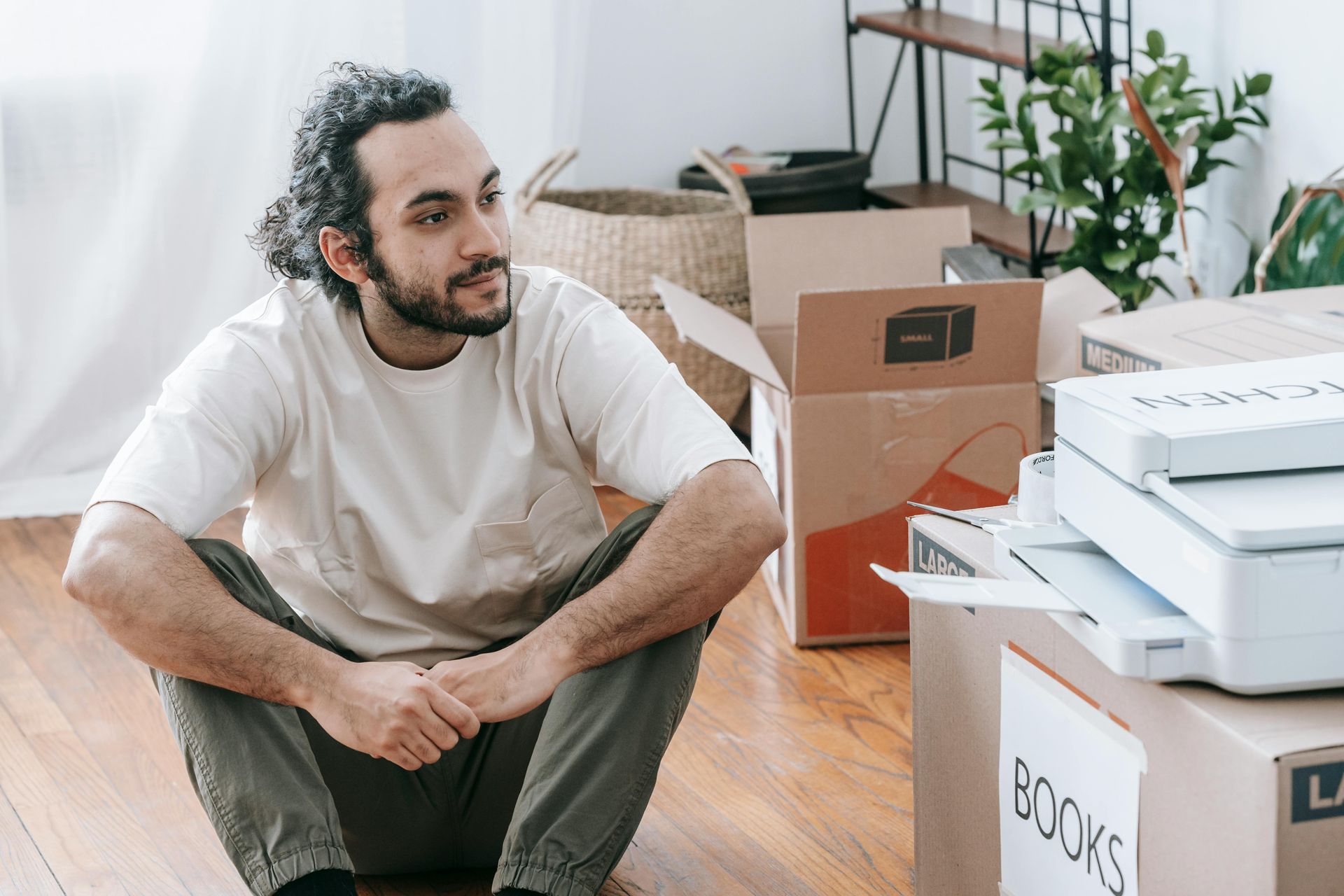Man sits on floor surrounded by moving boxes.
