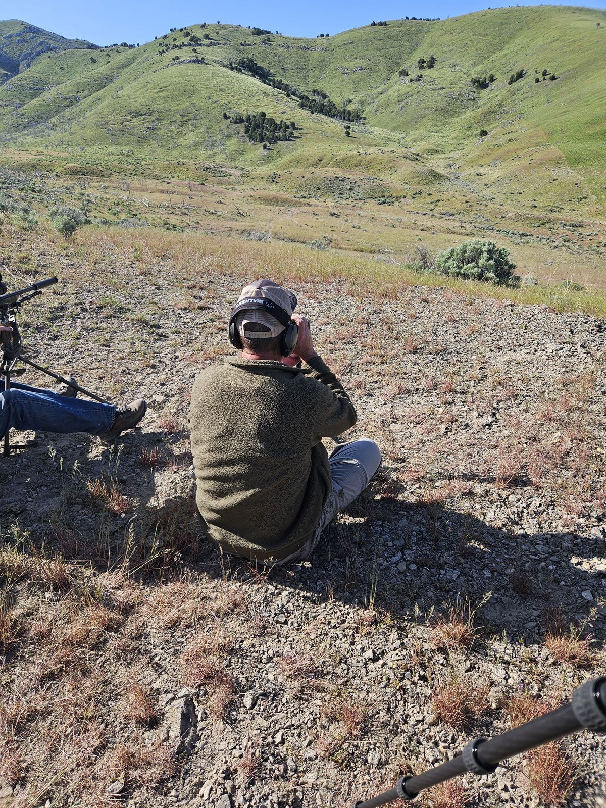 A man is sitting on the ground looking through binoculars.