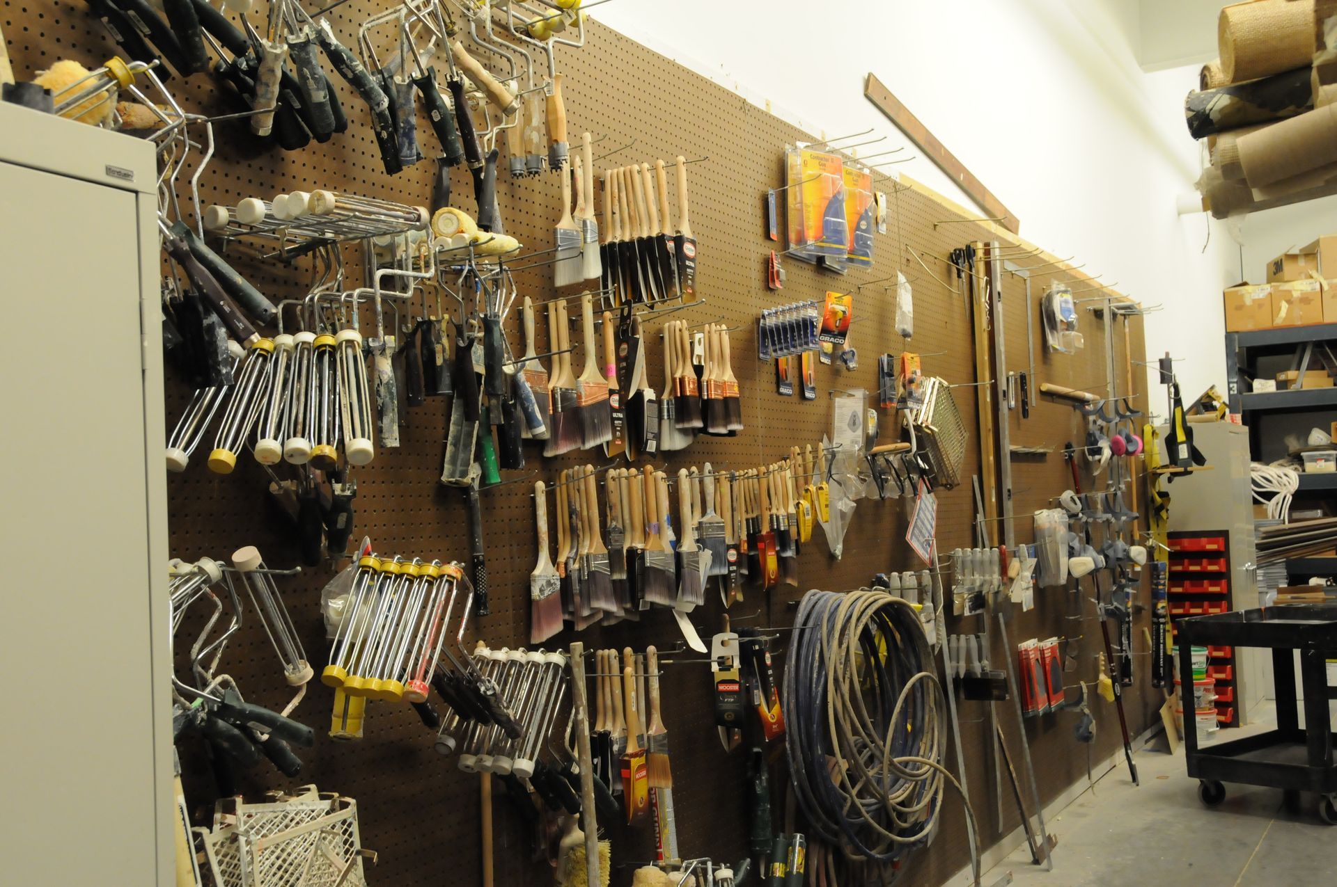 Organized tool wall at NCIFTI featuring brushes, scrapers, and rollers for professional finishing trades.