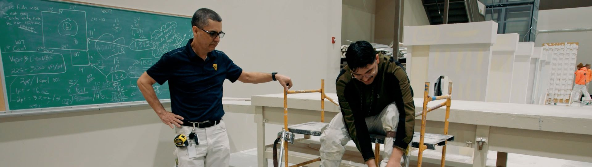 An NCIFTI instructor providing hands-on guidance to student practicing professional drywall taping and finishing.
