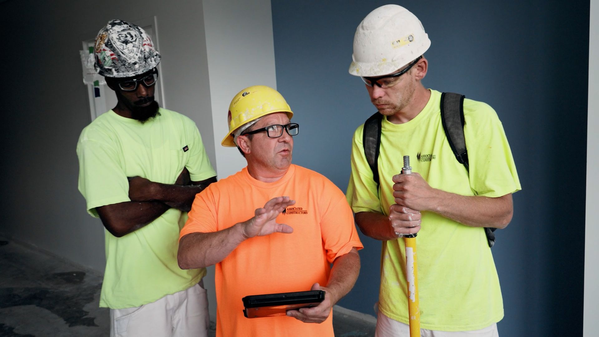A supervisor using a tablet to review project plants with two apprentices. 