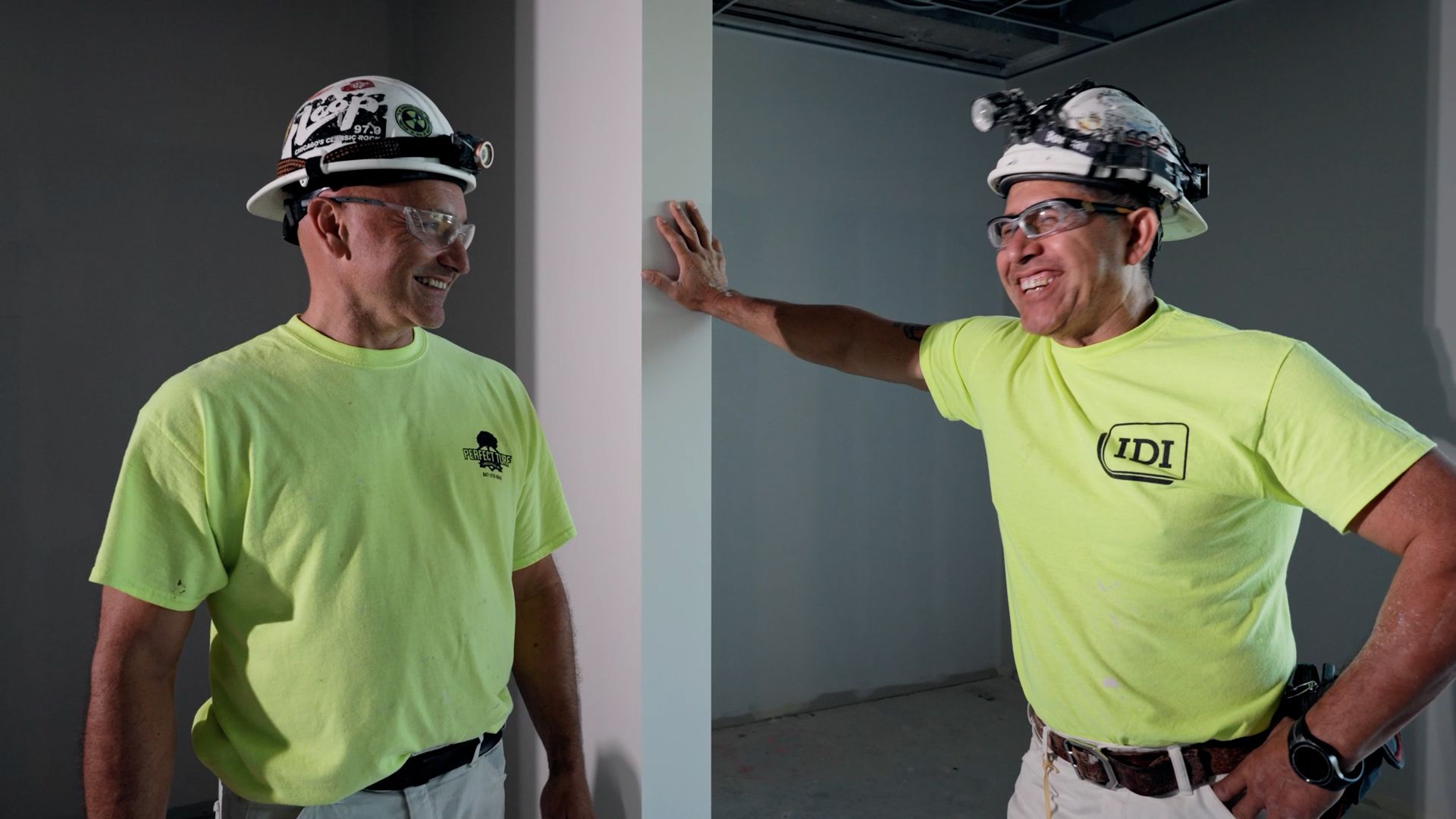Two tradespeople in high-visibility yellow shirts, hard hats, and headlamps on a job site.