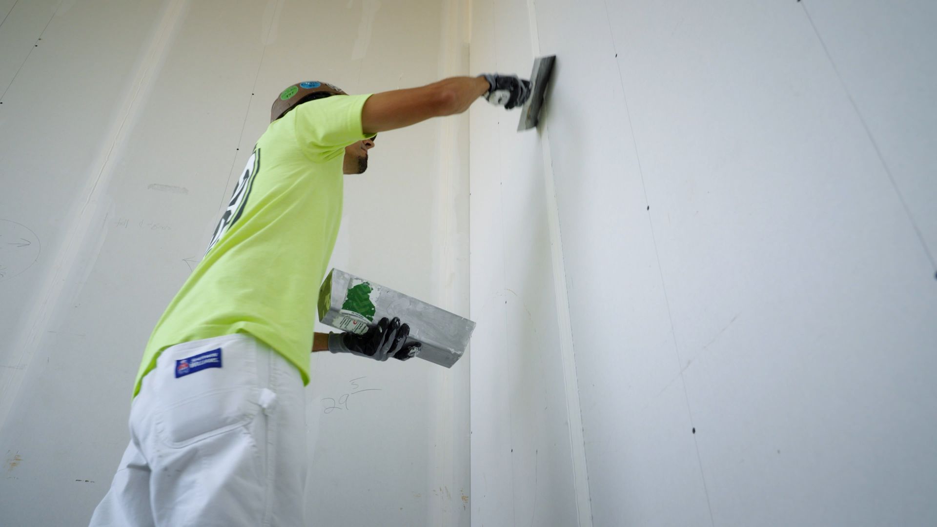 Low-angle view of a worker using a drywall knife and pan to smoot joint compound.