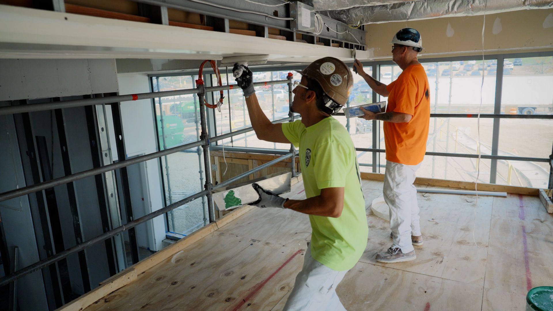 NCIFTI apprentices working on interior drywall finishing, with on student applying joint compound to a ceiling edge.