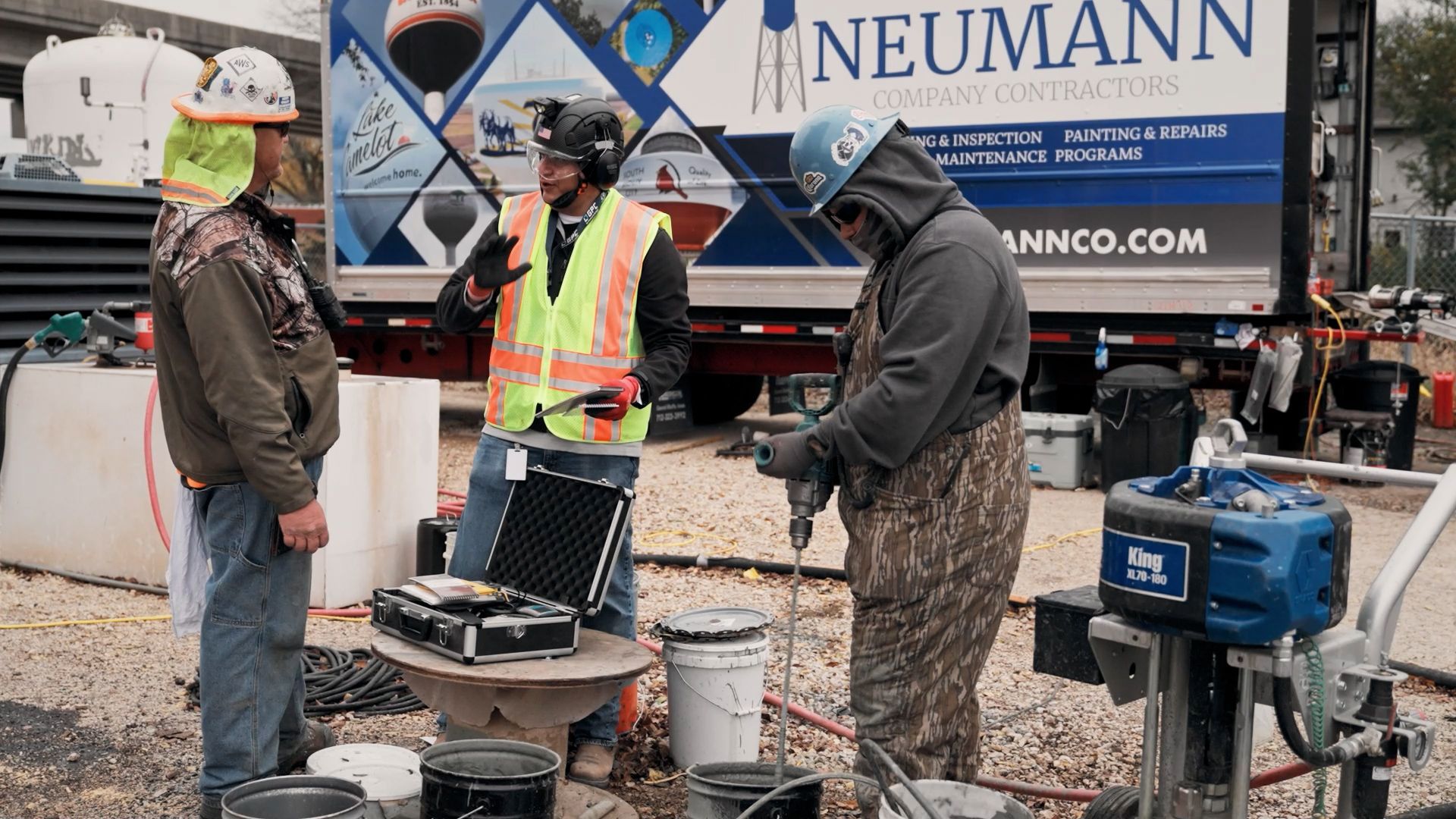 A group of painters in safety gear using high-powered mixing equipment at a job site.