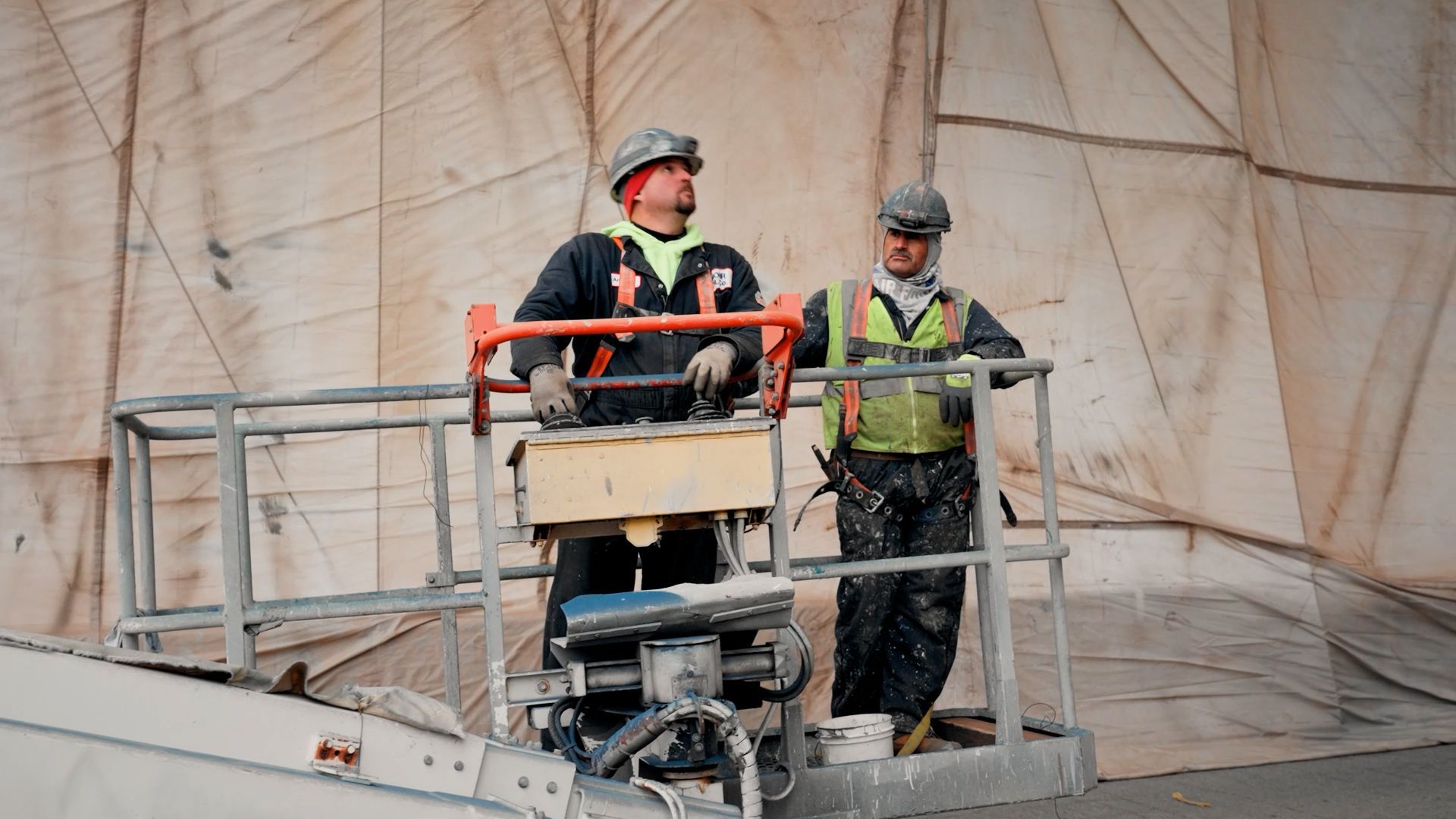 Two NCIFTI industrial painters operating a specialized mobile painting rig inside a large-scale containment area.