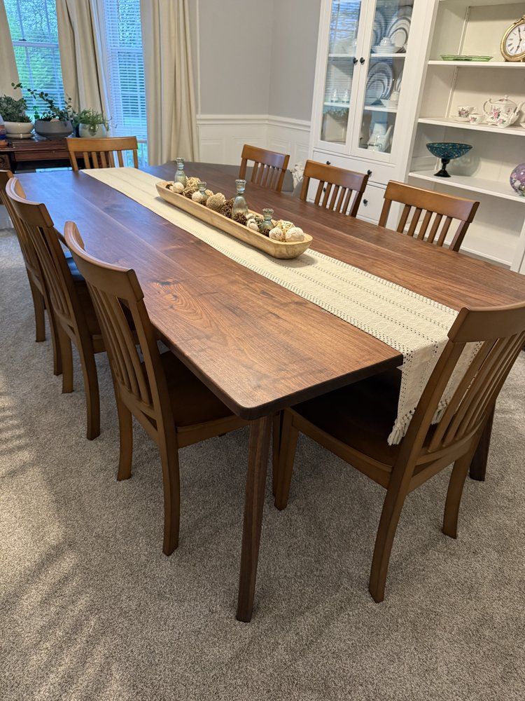 A long wooden dining table with chairs and a table runner in a dining room.