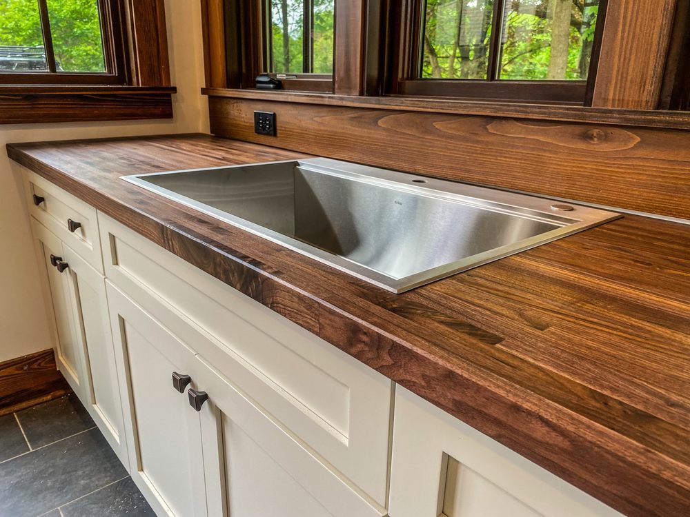 A kitchen sink with a wooden counter top and white cabinets.
