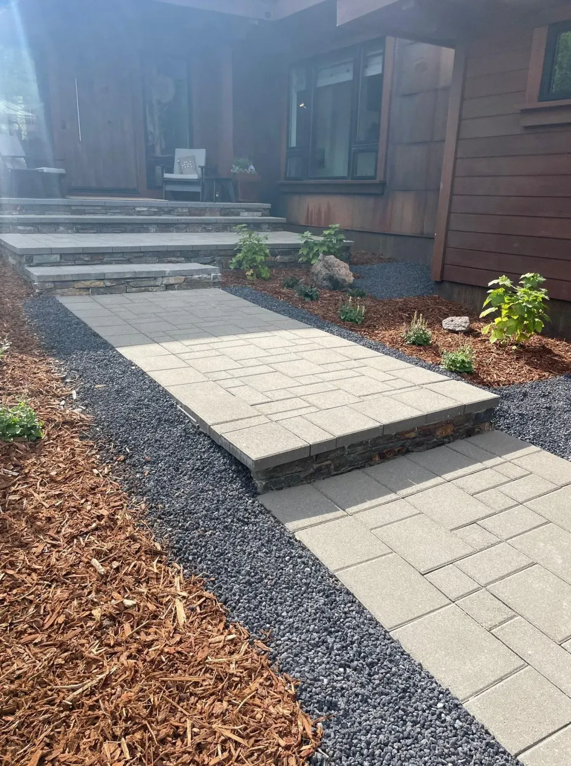 Stone walkway leading to a house with steps. Dark mulch on left, black rock on sides.
