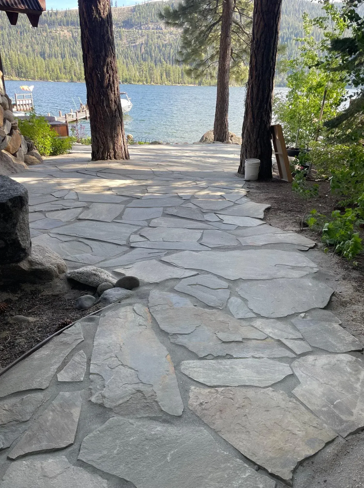 Stone path leading to a lake, flanked by trees and greenery.