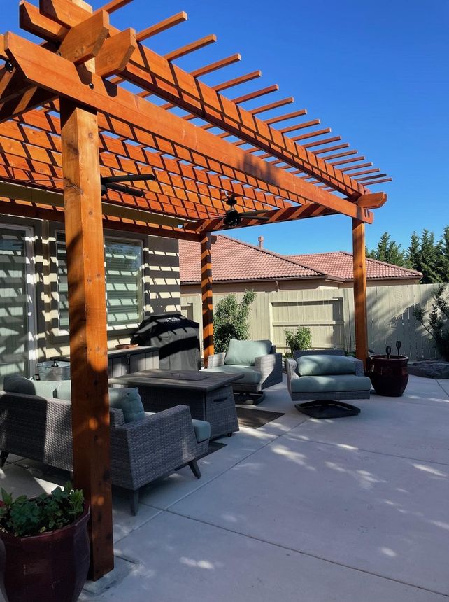 Wooden pergola over patio with outdoor seating on a sunny day.