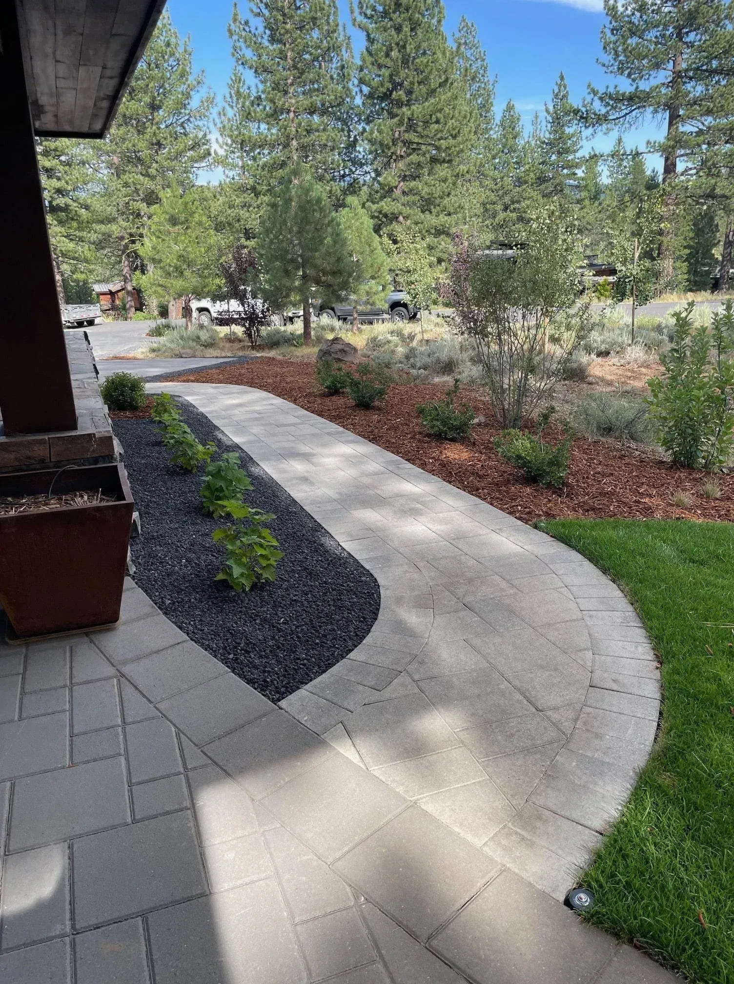 Paved walkway curves through a landscaped front yard with green grass, shrubs, and trees.