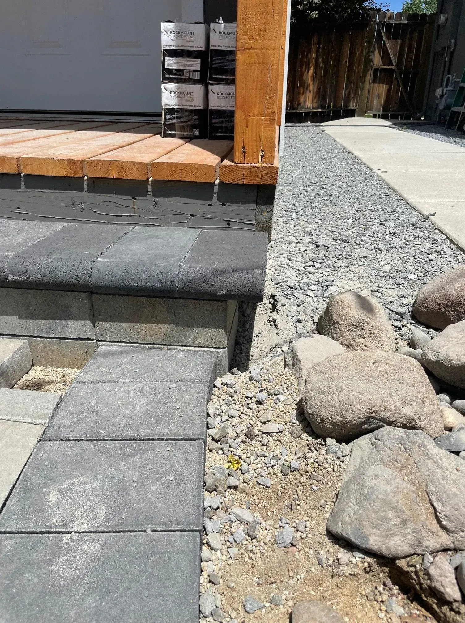Steps leading up to a wooden deck with stone pavers and a gravel path alongside.