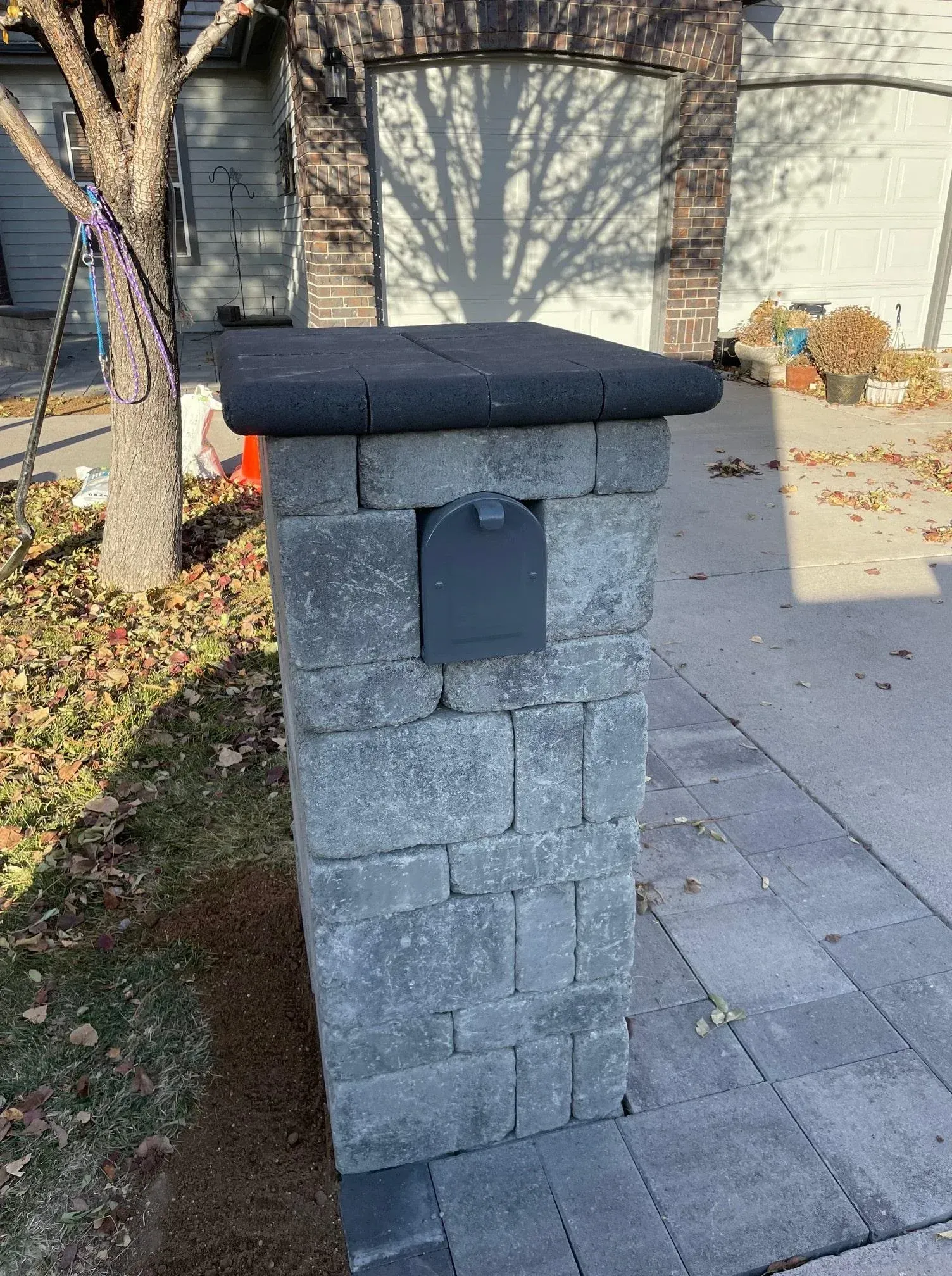 Stone mailbox with a black top and a grey mailbox door. Set in a driveway.