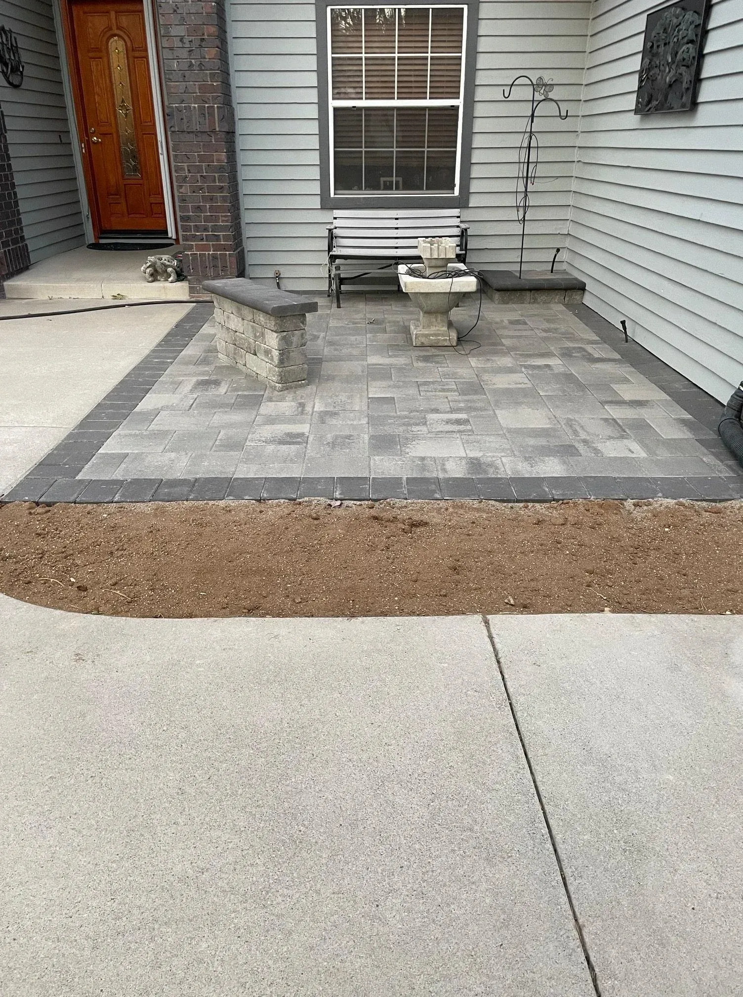 Patio with pavers and a small fountain in front of a house.