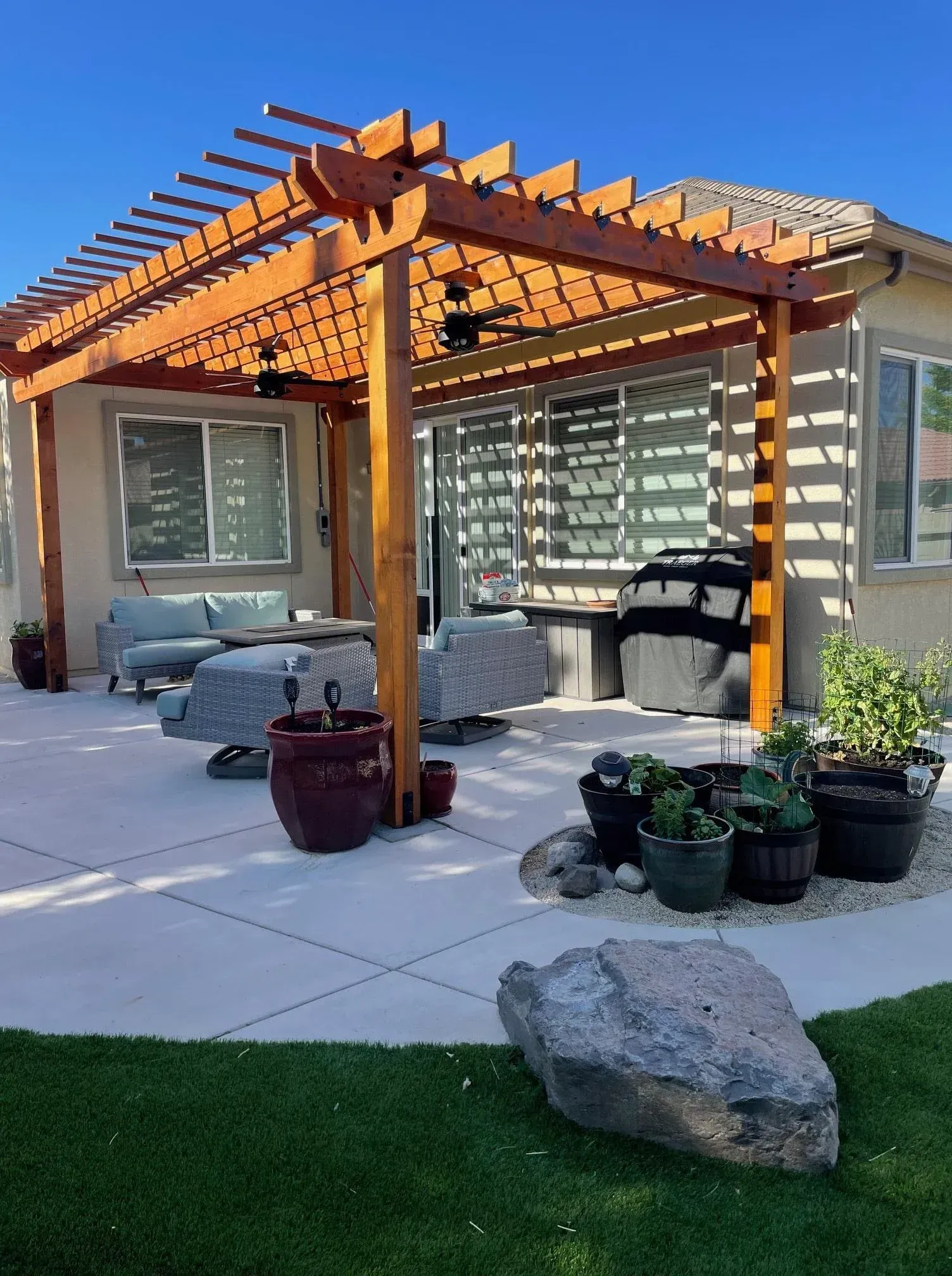 Wooden pergola over patio, with outdoor seating, plants, and grill.