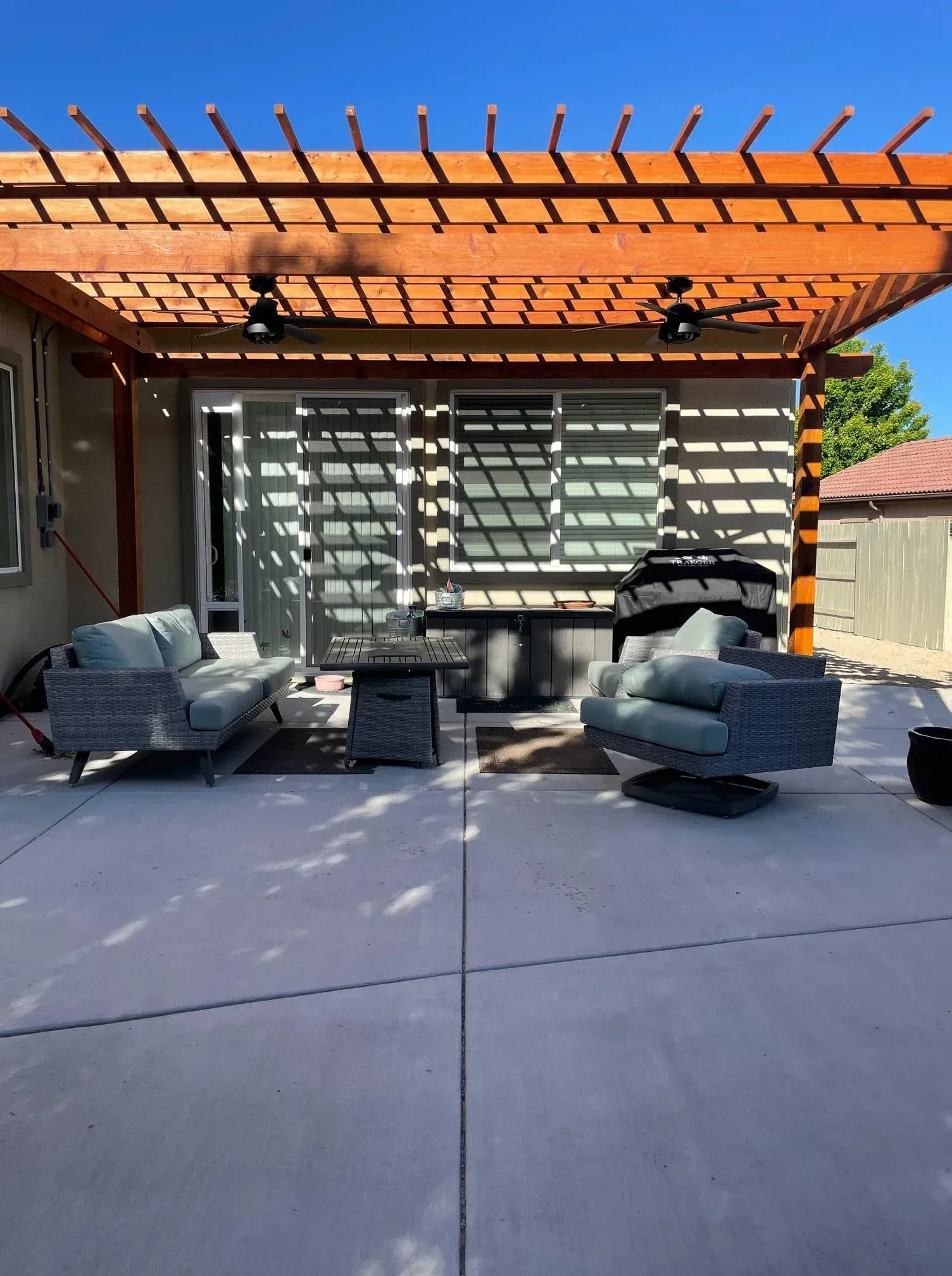 Patio with pergola, furniture, and a sliding glass door. Sunny day.