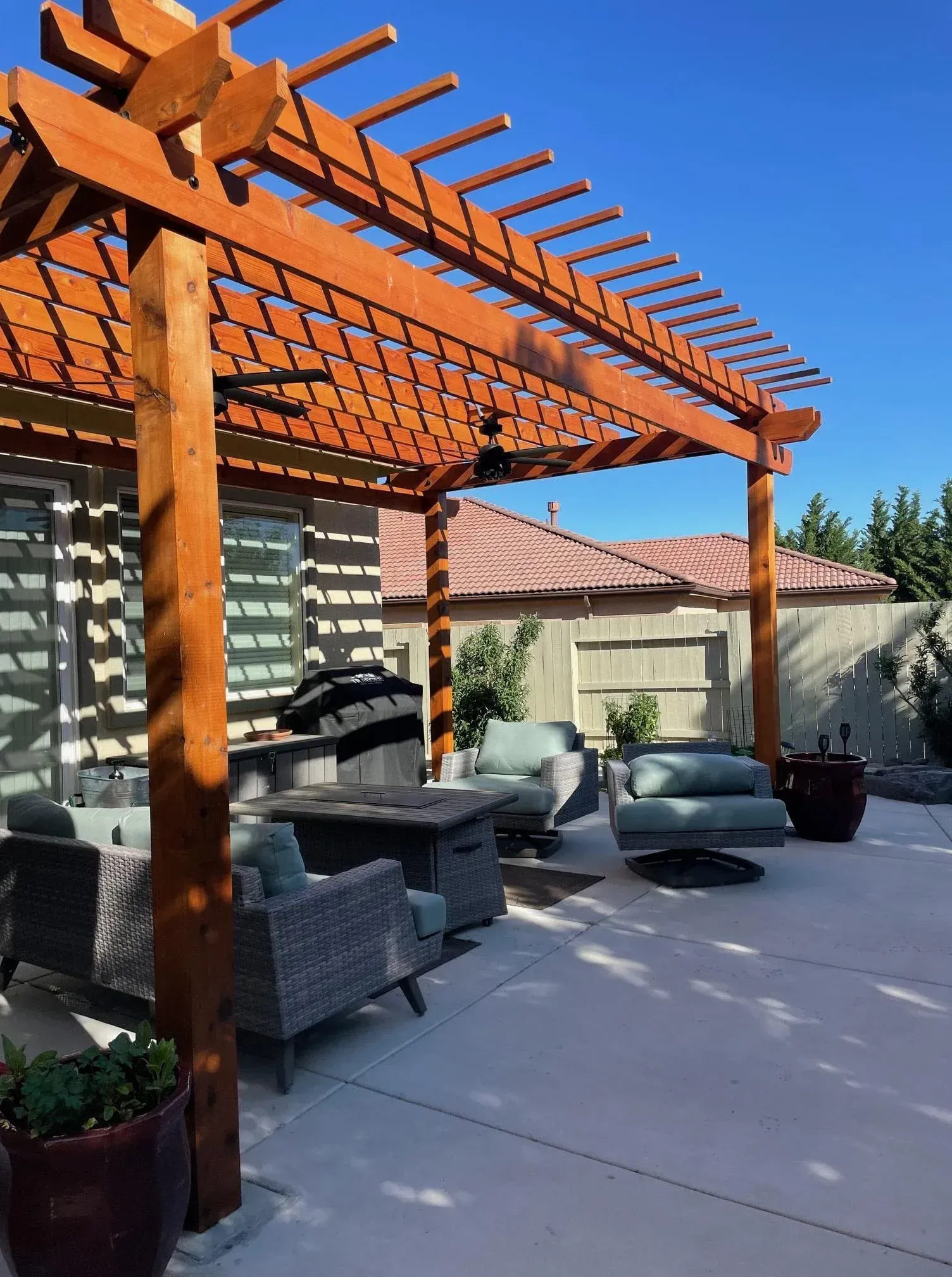Wooden pergola over a patio with seating, under a blue sky.