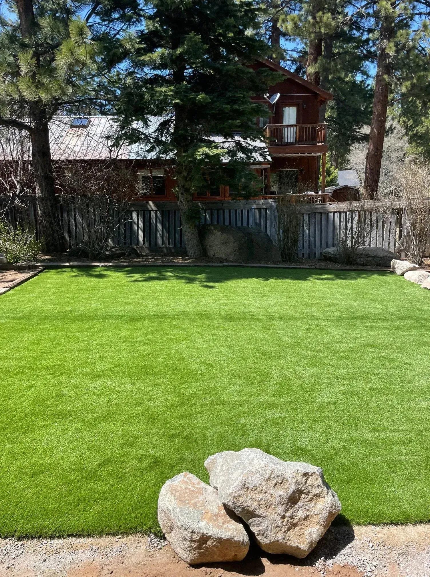 Lush green artificial lawn with two large rocks in front of a house with a treehouse.