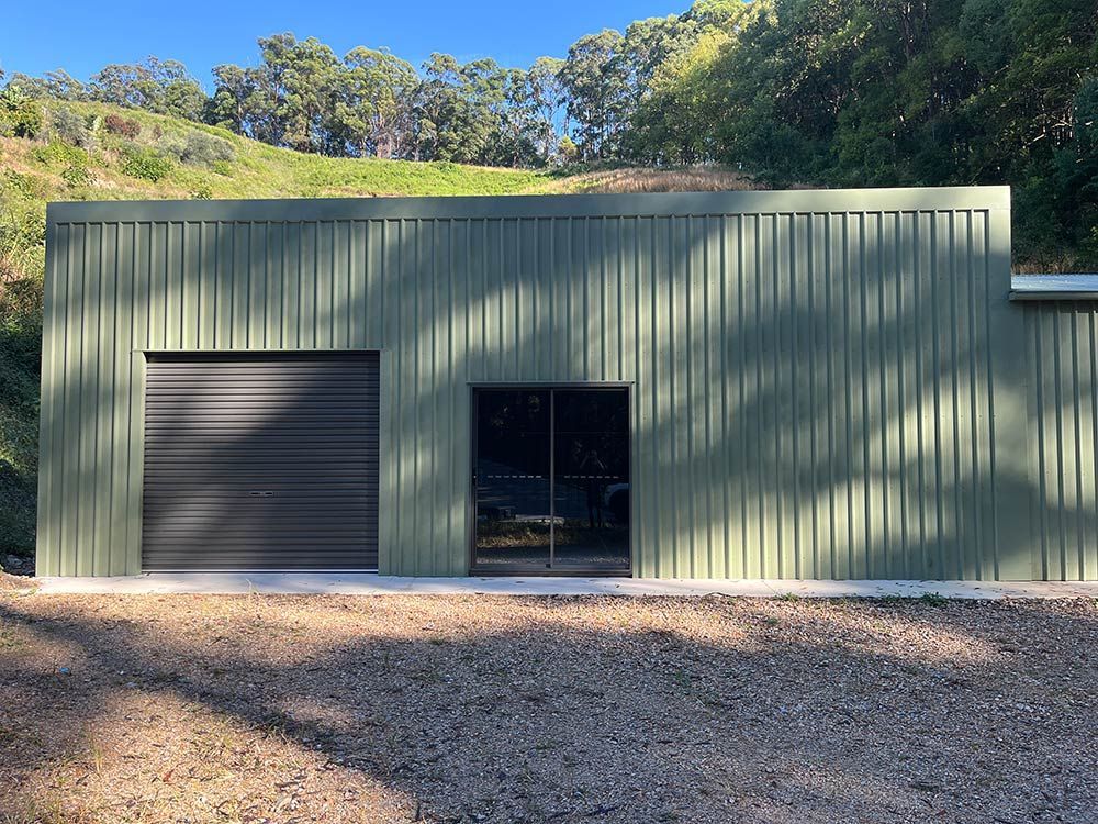 A Green Sheds With a Black Garage Door — Urbon Sheds in Uki, NSW