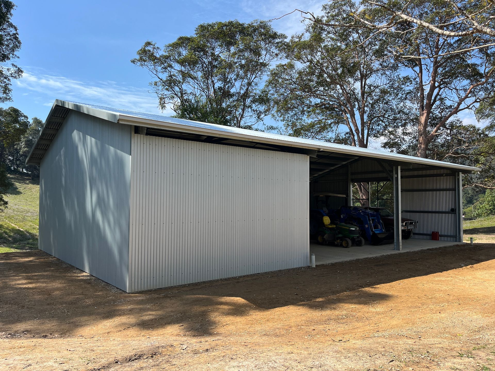 A Green Metal Sheds With A Concrete Driveway And Trees In The Background — Urbon Sheds in Casino, NSW
