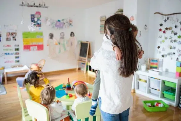 A woman holding a child in a brightly lit classroom filled with children and toys. A woman holding a child in a brightly lit classroom filled with children and toys.