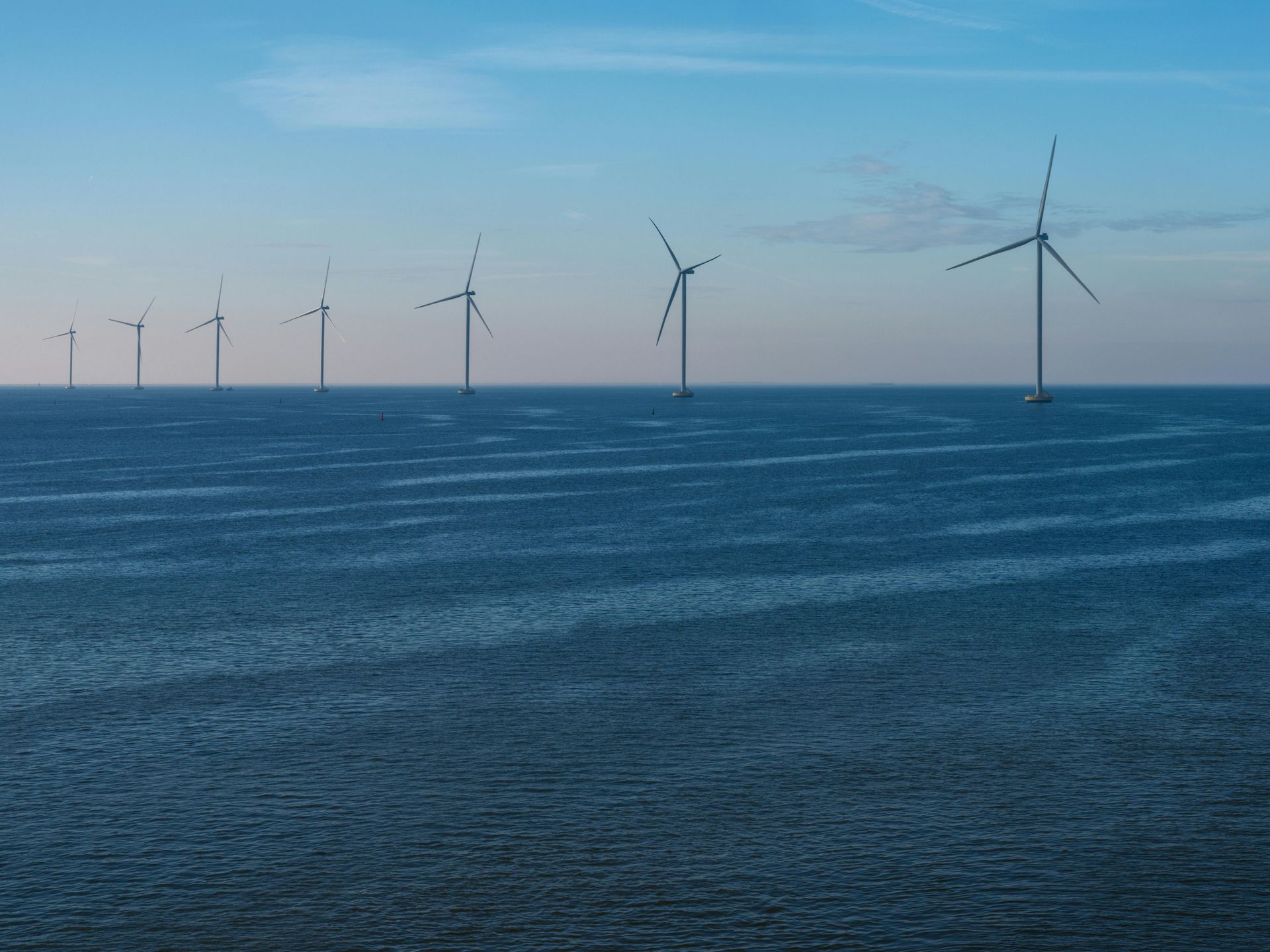Sunset over a harbor with cranes, a boat, and a ship. The sun reflects on the water.